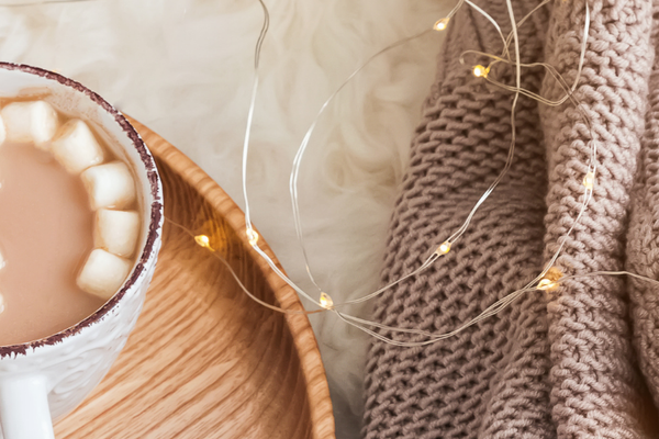 Hot cocoa, a candle, a wood tray, a warm throw blanket in a cozy setting - Celebratopia personalized gifting