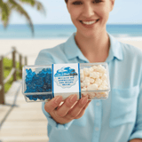 Person holding a container of blue and white candy with a beach background