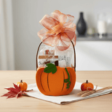 Pumpkin-shaped gift bag with a floral bow on a table with pumpkins and leaves.