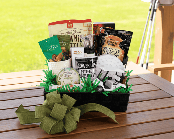 Golf themed gift basket with snacks on a wooden table with golf clubs in the background
