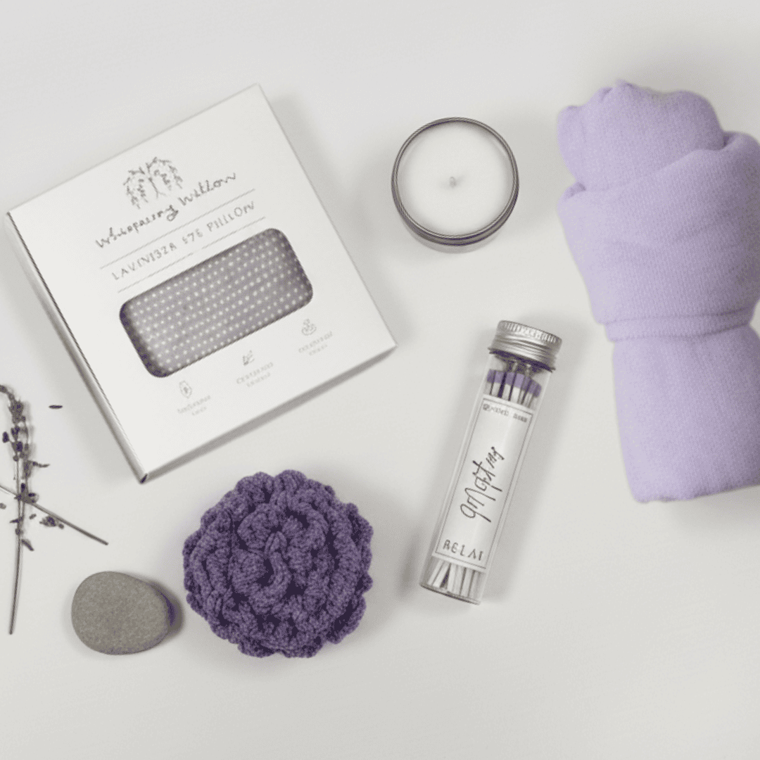 Relaxation products including an eye pillow, a candle and matches, a purple buffer pouf and a purple plush headband on a white background