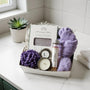 Bath gift set with purple towels, candle, and other items on a bathroom counter.