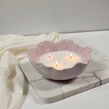 Lavender colored ceramic bowl with white wax pears and three lit wicks on a marble surface