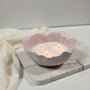 Lavender colored ceramic bowl with white wax pears and three lit wicks on a marble surface