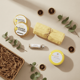 Collection of natural products including a yellow towel, shower steamers, and a jar on a beige background with eucalyptus leaves.
