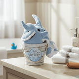 Blue shark-shaped towel in a bucket on a bathroom counter with towels and soap in the background