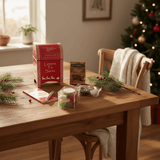 Wooden table with Christmas items including a red mailbox, pine sprigs, a holiday themed notepad and pen and holiday themed sweets