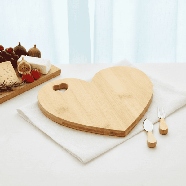 Heart-shaped wooden cutting board on a white surface with cheese and figs