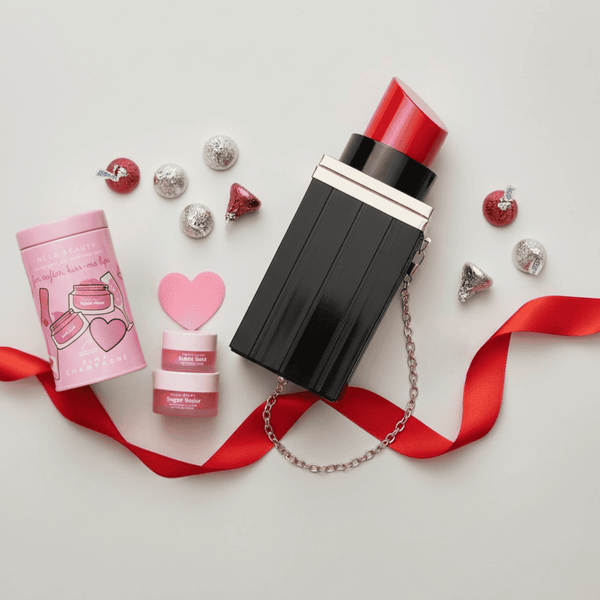 Black lipstick purse with pink lip spa product Hershey's Kisses with red ribbon on a light gray background