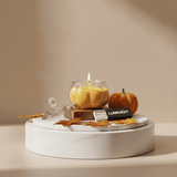 Decorative setup with a candle, pumpkin, and leaves on a white surface with a neutral background