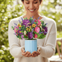 Person presents a Spring Floral Pop Up Card, featuring a vibrant bouquet in a blue pot, embodying the essence of everlasting Spring.