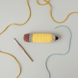 Crocheted pencil-shaped catnip kicker toy with yarn and a crochet hook on a light gray background