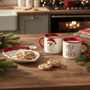 Two Santa mugs and a Santa plate, shown in a Christmas kitchen with cookies and milk