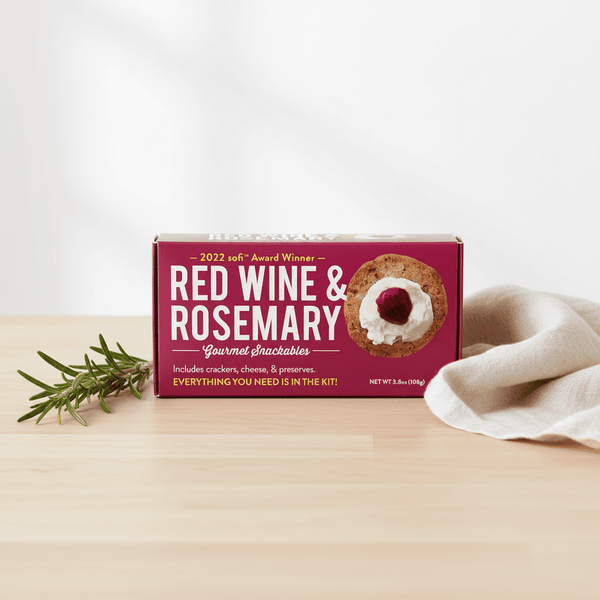 Box of Red Wine & Rosemary Gourmet Snackables on a wooden surface with a white background