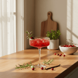 craftmix cranberry vanilla cocktail in a glass with garnishes on a wooden table, sunlit room.