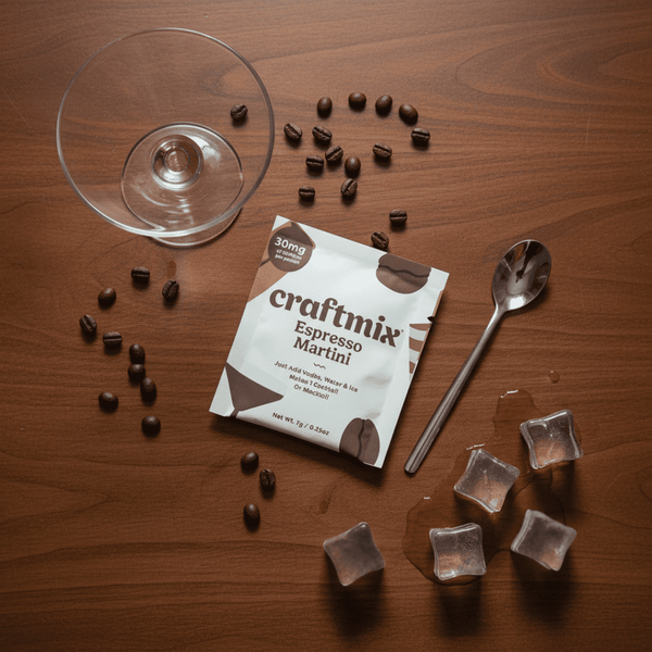Craftmix Espresso Martini mix packet with espresso beans, a glass, ice cubes, and a spoon on a wooden surface.