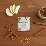 Craftmix Spiked Apple Cider package with apple slices, cinnamon sticks, and a mug on a wooden surface.