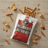Packaged Maple & Brown Butter pretzels on a wooden surface with pretzel pieces and syrup.