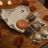 Halloween-themed treats on a ghost-shaped plate with autumn leaves on a wooden table.