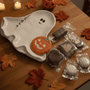 Halloween-themed treats on a ghost-shaped plate with autumn leaves on a wooden table.