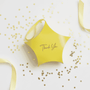 Yellow star shaped gift box with 'Thank You' on the front set on a white background with gold confetti and yellow ribbon