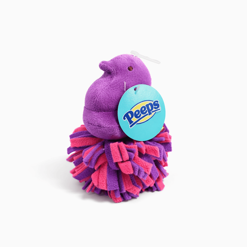Peeps Purple Chick Squeaky Fleece Dog Toy perched on a pink-and-purple pom-pom ball, featuring an attached Peeps logo tag, ideal for playful gifting.