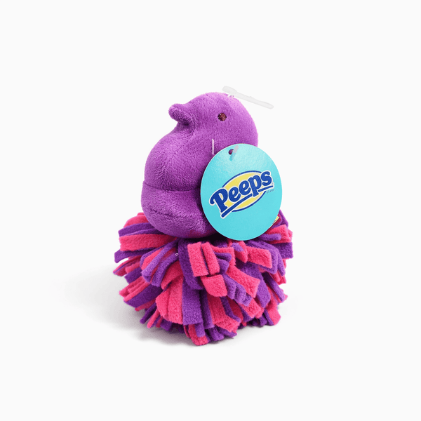 Peeps Purple Chick Squeaky Fleece Dog Toy perched on a pink-and-purple pom-pom ball, featuring an attached Peeps logo tag, ideal for playful gifting.